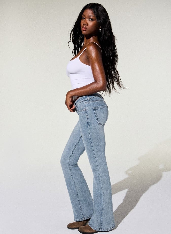 Model poses in a white tank top and light wash flared jeans.