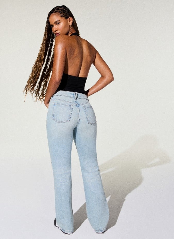Model poses in a black body suit and distressed light wash jeans.