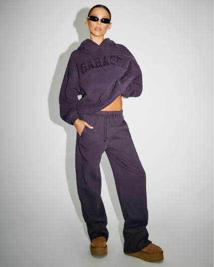 Hallie Batchelder wears a purple GARAGE hoodie, matching sweats, and black sunglasses.