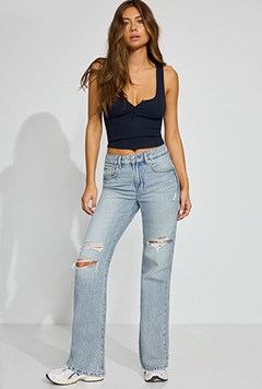 Model poses in a black tank top, distressed, light wash jeans, and sneakers.